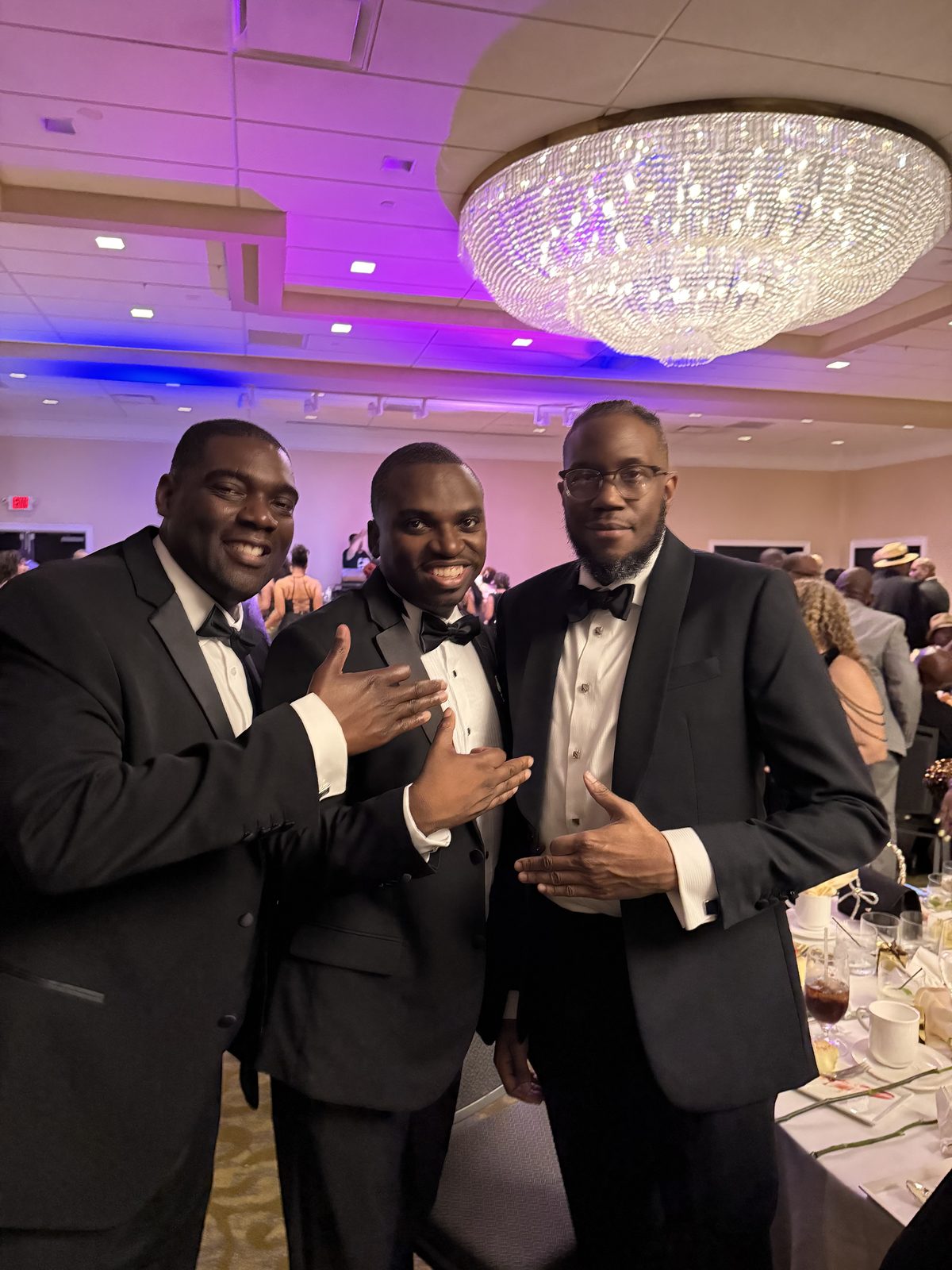 Three brothers in tuxedos beneath the ballroom chandelier